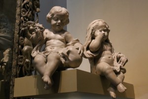 These macabre little cherubs are funerary decorations - each one is holding symbols of death. They're dark, real dark. 
